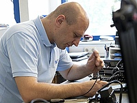 Service-Mitarbeiter in blauem Polo-Shirt sitzt an Tisch und arbeitet mit Werkzeug