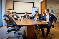 fünf Männer und eine Frau besprechen sich an Konferenztisch 