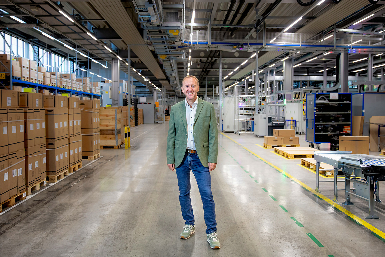 Martin Hackl posiert in Produktionshalle zwischen Kartons und Maschinen 